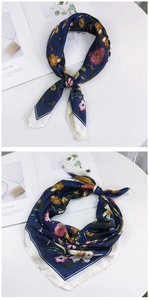 Detailed view of dark blue floral print silk scarf styled with elegant knots on white desk