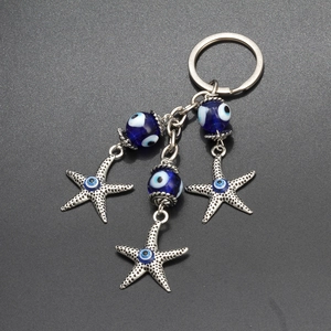Lucky blue evil eye keychain with silver starfish charms and glass beads on black surface