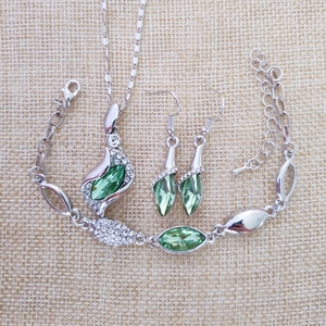 Flat lay of silver jewelry set with green marquise stones and clear crystals on beige cloth