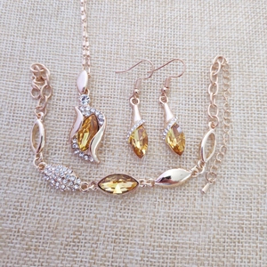 Rose gold jewelry set with yellow teardrop crystals and small diamonds on beige linen