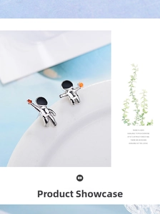 Detail of silver astronaut earrings with orange gemstone accent on ceramic edge