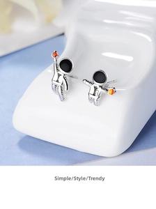 Macro shot of silver astronaut earrings with enamel details on a white textured stand