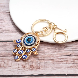 Close-up of a golden Hamsa Hand keychain with blue evil eyes and sparkling rhinestones