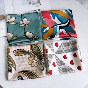 Assorted square silk scarves with floral, paisley and geometric patterns on a white table