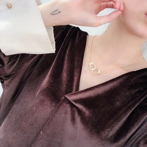 Detail of a gold handcuff pendant necklace worn by a model on dark velvet fabric