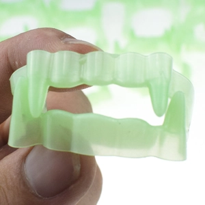 Close-up of luminous green vampire fangs for Halloween costume held by fingers