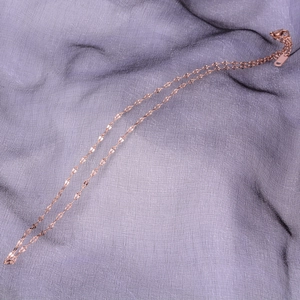 Close-up of a rose gold flat link necklace with clasp on purple textured fabric