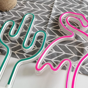 Top view of neon LED lamps in green cactus and pink flamingo shapes on a grey fabric
