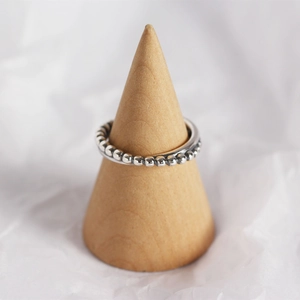 Detail of silver beaded ring on wood cone stand with soft textured background