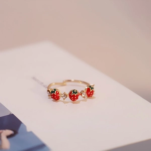 Macro detail of gold strawberry ring with red enamel charms and sparkling crystals