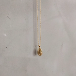 Detailed macro view of minimalist gold seashell pendant with fine spiral texture on gray stone