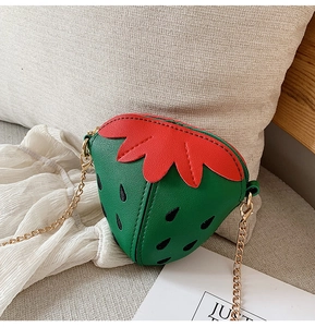 Detailansicht der Erdbeere Umhängetasche aus PU-Leder mit goldener Kette auf einem Kissen