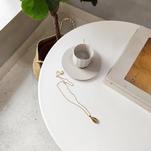 Detailed view of a gold shell pendant necklace elegantly placed on a white table surface