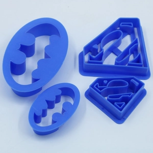 Blue plastic cookie cutter set featuring Superman and Batman logo silhouettes for baking