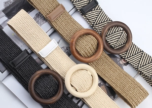 Detail of four bohemian elastic straw belts with round wooden buckles in earthy tones
