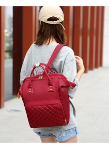 Burgundy quilted nylon travel backpack for moms shown being worn in a modern outdoor setting