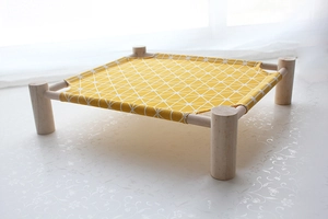 Detail view of the raised pet cot showing yellow canvas fabric and sturdy wood frame