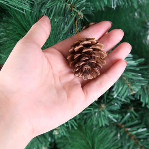 Natural pine cone ornament held in hand for size reference with gold hanging string