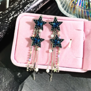 Close-up of star-shaped earrings with blue crystals, pearl tassels and silver chains