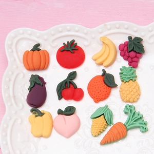 Dettaglio di dodici ciondoli in resina a forma di frutta e verdura colorata in un piatto bianco