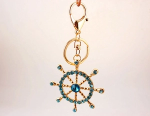 Close-up of golden nautical helm keychain with sparkling blue crystals and lobster clasp