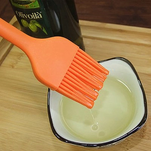 Orange one-piece silicone oil brush for BBQ and baking shown with oil bowl and olive oil