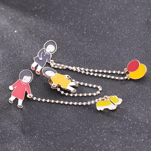 Close-up of enamel cartoon girl brooches with pearl chains on a grey background