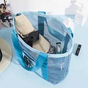 Blue mesh beach tote bag with shoulder straps and summer travel accessories on blue background