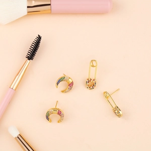 Close-up of golden crescent moon and safety pin earrings with rainbow zircon stones