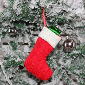 Mini red knitted Christmas stocking with white cuff and green gift hanging on tree