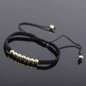 Macro shot of black woven rope bracelet with seven polished gold beads and pull string detail