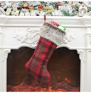 Close-up of red and green plaid Christmas stocking with faux fur trim by a cozy fireplace