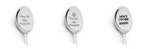 Close-up of three engraved stainless steel coffee spoons with sentimental messages