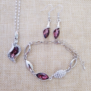 Detail of silver jewelry set with purple marquise crystals on beige linen background