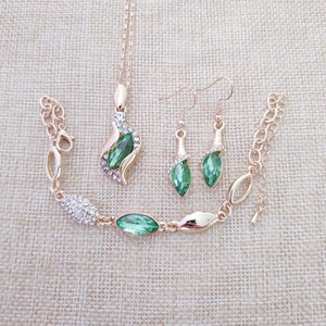 Detailed view of gold jewelry set featuring green leaf crystals and clear rhinestones