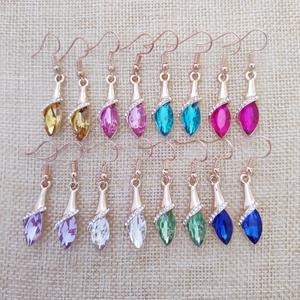 Close-up of teardrop crystal earrings in multiple colors with golden hooks on linen