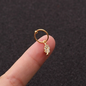 Dettaglio di un orecchino a foglia dorata con zircone tenuto sulla punta delle dita