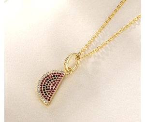 Detail of a golden necklace featuring a vibrant watermelon pendant with colorful zircon stones