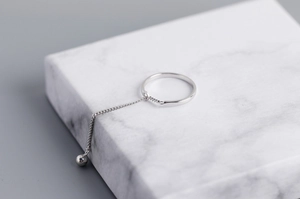 Detail view of S925 sterling silver chain ring with hanging bead on marble base