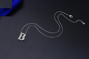 Macro shot of S925 silver letter B pendant with sparkling diamonds on a grey surface