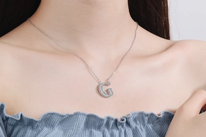 Close-up of a silver chain with a sparkling rhinestone-encrusted letter G pendant