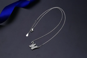 Macro view of silver letter W pendant featuring sparkling crystals on a fine link chain