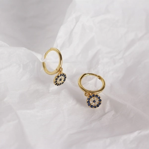 Macro view of gold hoop earrings with sparkling blue evil eye charm on pleated paper