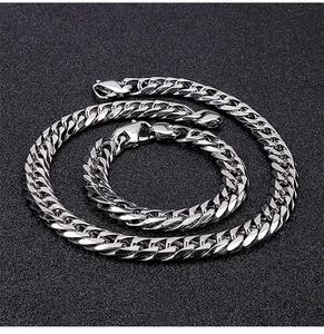 Close-up of polished silver stainless steel Cuban link necklace and bracelet set on black background