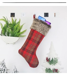 Detail of plaid Christmas stocking with plush cuff and gift boxes hanging on wall