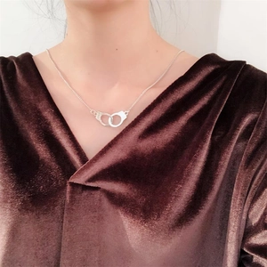 Detail of silver handcuff pendant necklace on a model with a dark velvet background