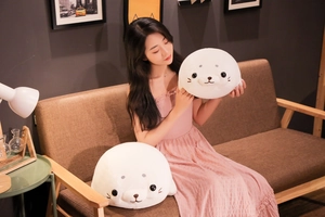 Lifestyle shot of two sizes of plush white seal pillows held by a woman on a sofa