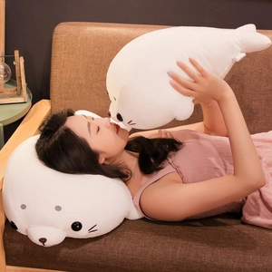 Cute white seal plush toy pillows in two sizes shown on a cozy sofa setting