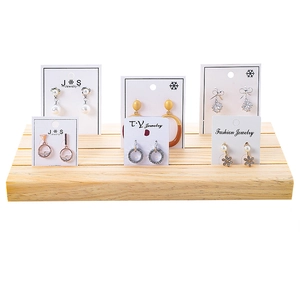 Wooden earring display stand with tiered slots and jewelry cards in a minimalist setting