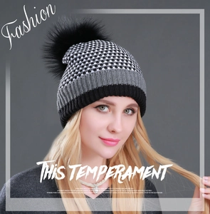 Detailed close-up of knit winter beanie with black raccoon fur pompom and tricolor texture